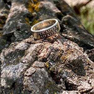 May include: A silver ring with the inscription "Per aspera ad astra" on a tree branch.