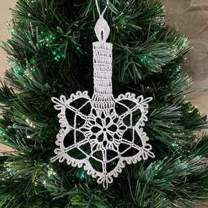 May include: White crocheted snowflake ornament with a white crocheted candle hanging from a Christmas tree.