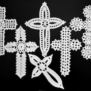 May include: A selection of six white, crocheted crosses in diverse designs against a black backdrop. The crosses showcase complex openwork patterns, with some featuring floral or geometric centres. The handmade crosses are presented as a group.