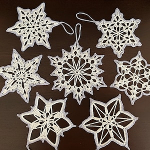 May include: Eight white crocheted snowflake ornaments with a delicate, lacy design. Each snowflake has a loop for hanging.