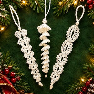 Könnte beinhalten: Drei weiße Häkelornamente mit komplizierten Spitzenmustern und kleinen Perlenakzenten. Jedes Ornament verfügt über eine geflochtene Schlaufe zum Aufhängen. Die Designs umfassen eine blattartige Form, einen spiralförmigen Eiszapfen und eine Kette.