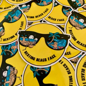 May include: A yellow sticker with a smiley face wearing sunglasses. The sunglasses reflect a beach scene with a palm tree, ocean waves, and a person laying on a beach towel. The text "RESTING BEACH FACE" is written in black letters on the sticker.