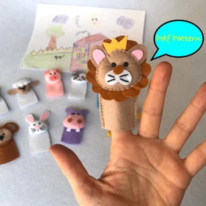 May include: A set of felt finger puppets featuring a lion, pig, sheep, dog, monkey, rabbit, and hippopotamus. The lion puppet is wearing a gold crown and is on a hand with the text "Pdf Pattern" in a speech bubble.