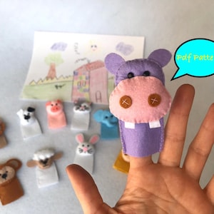 May include: A set of felt finger puppets featuring various animals, including a lion, a dog, a pig, a cat, an elephant, a rabbit, a sheep, a monkey, and a hippopotamus. The puppets are purple, pink, brown, white, and gray. The image also includes a drawing of a house and a sun. The text "Pdf Pattern" is in a blue speech bubble.