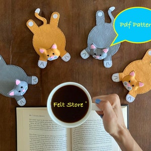 May include: Four felt cat coasters, two gray and two orange, with pink noses and white paws. The coasters are arranged around a cup of coffee and a book. The text "Pdf Pattern" is written on a blue speech bubble. The text "Felt Store" is written on the cup.