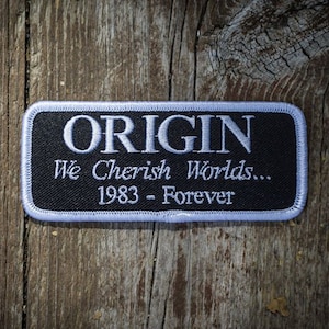 Puede incluir: Parche bordado en blanco y negro con texto blanco que dice "ORIGIN We Cherish Worlds... 1983 - Forever".