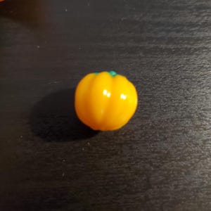 May include: A single, bright yellow bell pepper with a green stem. The pepper is sitting on a dark surface.