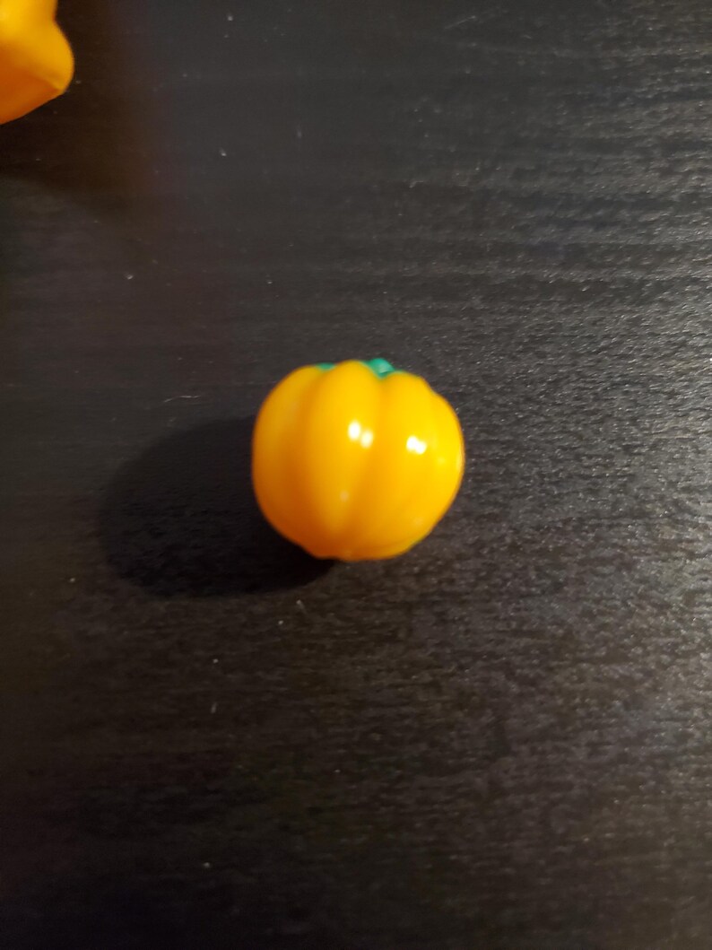 May include: A single, bright yellow bell pepper with a green stem. The pepper is sitting on a dark surface.