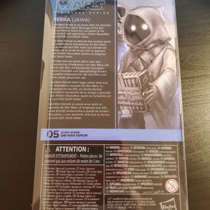 May include: A Star Wars: The Black Series action figure of Teeka, a Jawa from the Star Wars universe. The figure is packaged in a clear plastic box with a black and white background. The box features a photo of Teeka and text about the character. The text on the box reads "Star Wars: The Black Series Teeka (Jawa)".