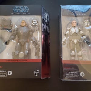 May include: Two action figures from Star Wars: The Black Series, in their original packaging. One figure is Wrecker, the other is Tech. Both figures are in clear plastic boxes with the Star Wars logo and warning labels.