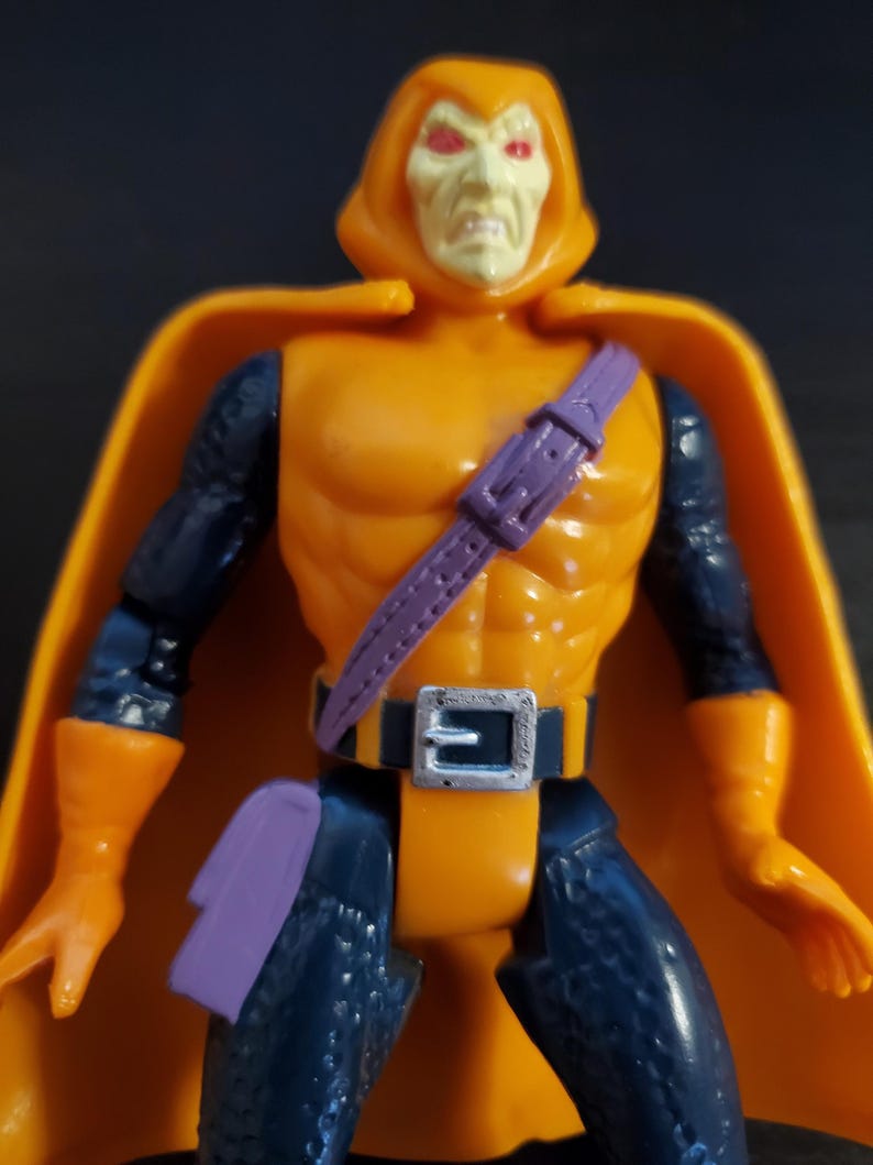 May include: An orange and blue action figure of the Marvel Comics villain, the Hobgoblin. The figure has a purple belt and a purple pouch on its leg. The figure has a yellow hood with a red face and red eyes.