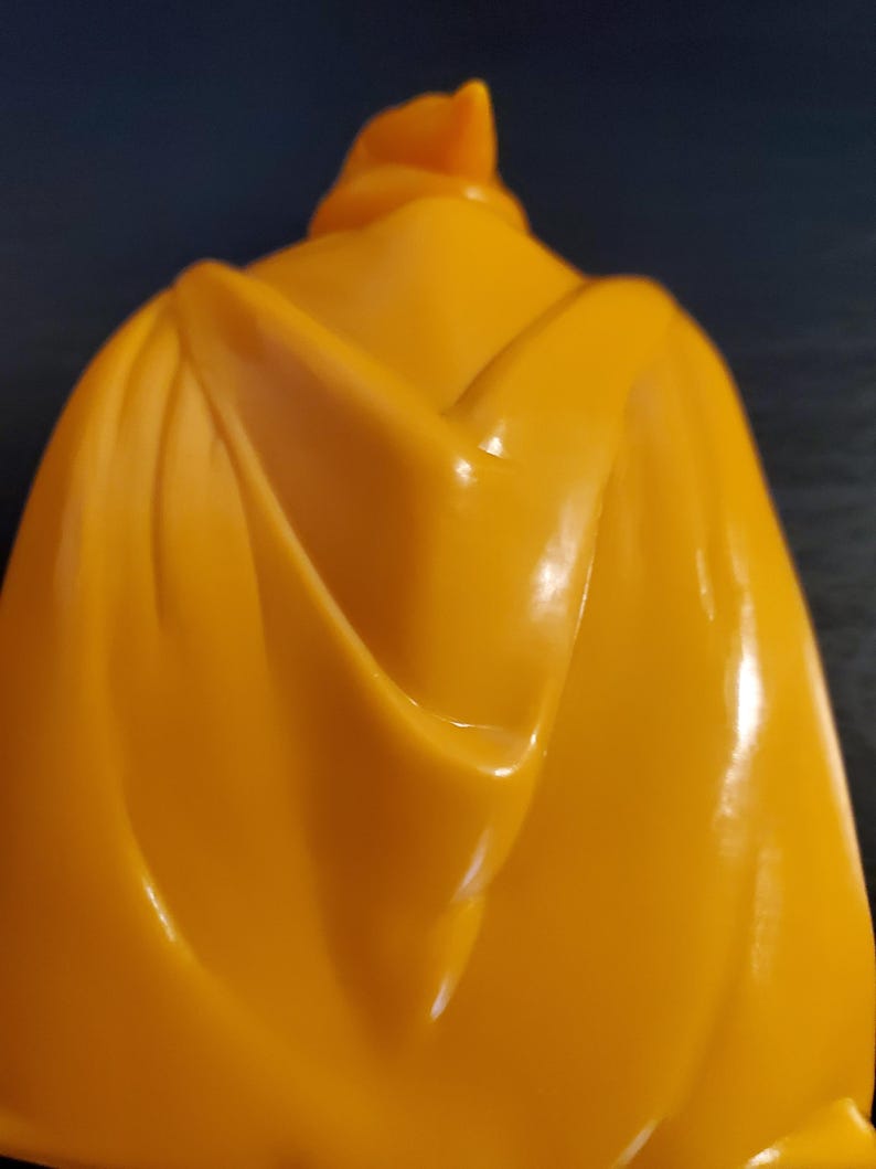 May include: A yellow plastic cape with a smooth, shiny finish. The cape is folded in the back, creating a dramatic look.