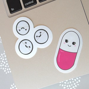 May include: A collection of stickers featuring cartoon pill designs. One sticker shows a pink and white capsule with a smiling face. Another sticker has three white pills with different facial expressions.