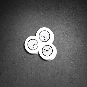 May include: A cluster of three white, circular objects with cartoon faces. Each object has a different expression: one is smiling, one is neutral, and one is frowning. The objects are arranged in a cloverleaf pattern against a dark gray background.