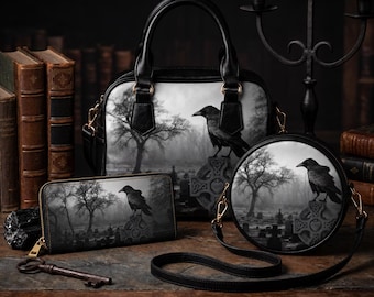 May include: A black handbag, a rectangular wallet, and a round crossbody bag, each featuring a monochromatic print of a raven perched on a stone cross in a misty graveyard. The set includes black handles, straps, and gold-toned hardware.