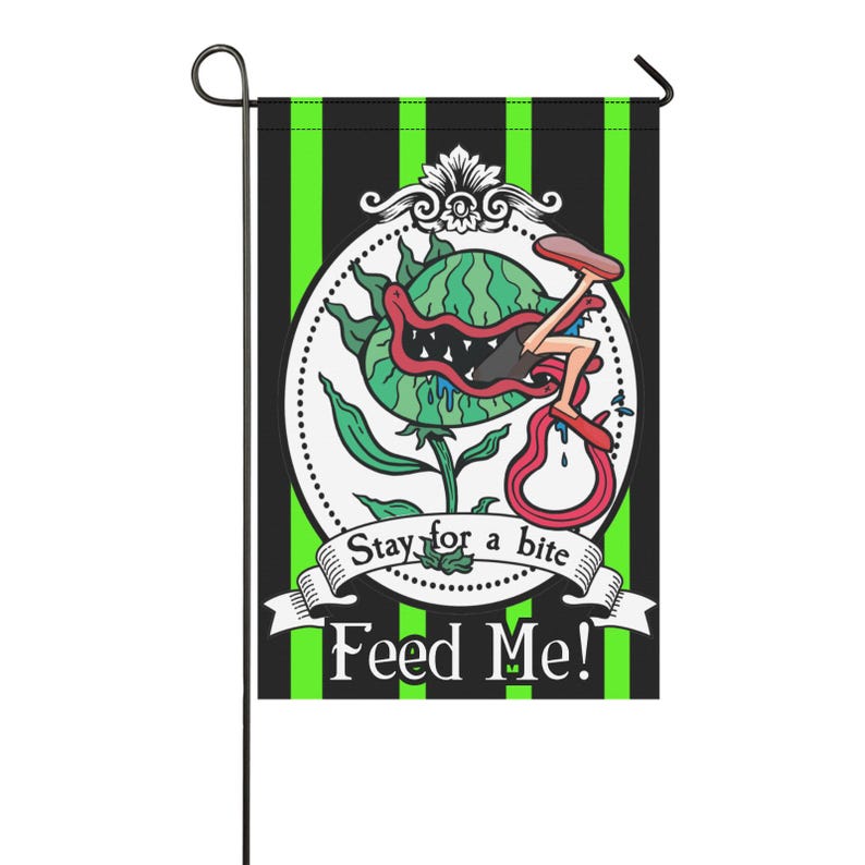 May include: A decorative garden flag featuring a cartoon illustration of a Venus flytrap with a person being eaten. The flag has a black and green striped background with the text "Stay for a bite" and "Feed Me!"