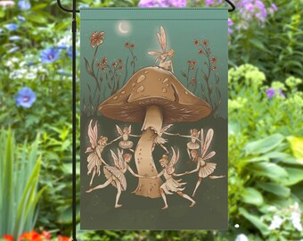 May include: A garden flag with a whimsical design featuring fairies dancing around a large mushroom. The mushroom is brown with a white stem and the fairies are wearing colorful dresses with wings. The background is a green and blue gradient with flowers and leaves.