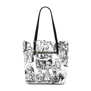 Puede incluir: Una bolsa de mano de lona negra y blanca con un estampado de ilustraciones de Alicia en el Pa&iacute;s de las Maravillas. La bolsa tiene asas negras y una cremallera dorada.