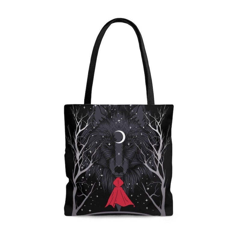 Puede incluir: Bolsa de tela negra con la cabeza de un lobo y una luna creciente en el centro. La cabeza del lobo est&aacute; rodeada de un cielo nocturno estrellado y &aacute;rboles. Una peque&ntilde;a figura con una capa roja con capucha se encuentra frente a la cabeza del lobo.