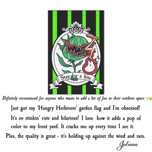 May include: A garden flag with a black and green striped background. The flag features a cartoon illustration of a plant with a mouth and the text "Stay for a bite". The plant is green, red, and white.