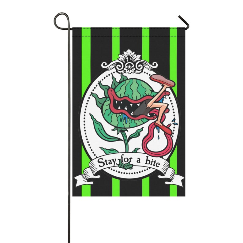 May include: A garden flag with a black and green striped background. The flag features a cartoon illustration of a plant with a mouth and legs, with the text "Stay for a bite" on a banner.
