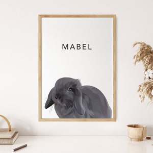 Op de afbeelding: Een ingelijst afdruk van een grijs konijn met de naam Mabel in zwarte tekst bovenaan de afdruk.