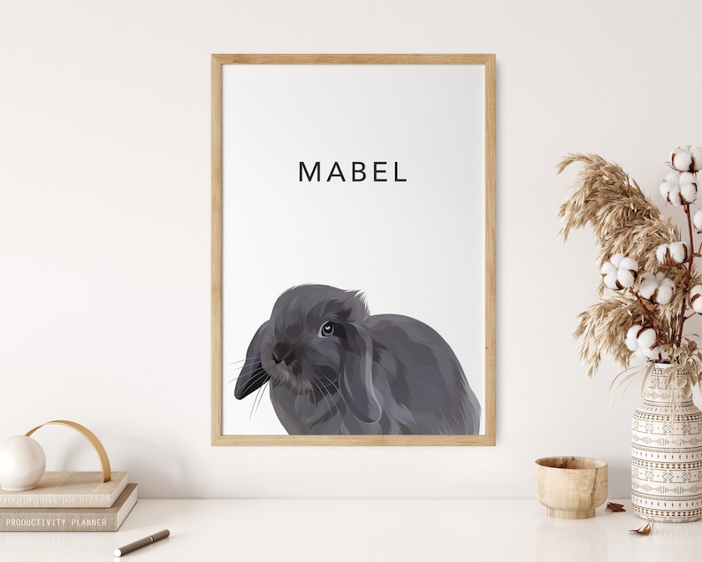 Op de afbeelding: Een ingelijst afdruk van een grijs konijn met de naam Mabel in zwarte tekst bovenaan de afdruk.