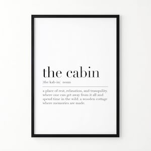 May include: A framed wall art print featuring a dictionary-style definition of the word the cabin. The text reads: the cabin [the kab-in] noun a place of rest, relaxation, and tranquility. where one can get away from it all and spend time in the wild, a wooden cottage where memories are made.