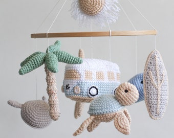 May include: A crocheted baby mobile with a wooden ring, featuring a palm tree, a surfboard, a turtle, a van, and a sun with white fringe.