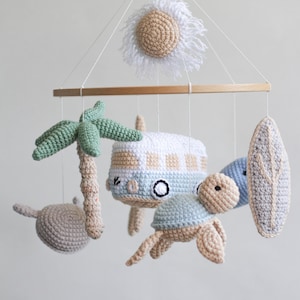 Op de afbeelding: Een gehaakte babymobiel met een houten ring, met een palmboom, een surfboard, een schildpad, een busje en een zon met witte franjes.