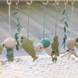 May include: A wooden baby mobile with crocheted sea creatures, including a starfish, jellyfish, shark, turtle, octopus, and a pufferfish. The mobile is hanging from a wooden frame.