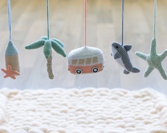 May include: A wooden baby play gym with a white crocheted mat and five hanging crocheted toys: a palm tree, a camper van, a shark, a starfish, and a bottle with a starfish on top.
