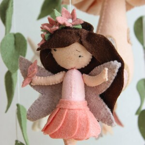 May include: A felt fairy mobile featuring a pink mushroom, green leaves, and a pink fairy with brown hair and pink wings.