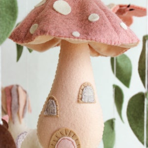 May include: A pink felt mushroom with white polka dots and a small house-shaped stem. The mushroom has two windows and a door.