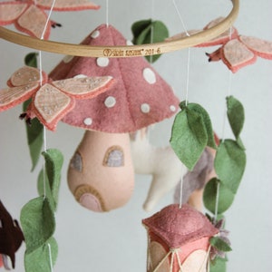 May include: A pink and white felt mushroom mobile with a small house, a lantern, butterflies, and leaves. The mobile is hanging from a wooden ring and has the text "Sril Kasimir 201-6" on it.