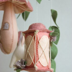 May include: A pink felt lantern with a white rope design hangs from a mobile. The lantern has a pink flower on the side.