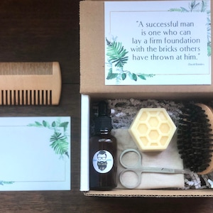 May include: A gift box set for beard care with a wooden comb, beard oil, beard balm, a brush, scissors, and a small cloth. The box is brown with a white lid and a quote on the lid that reads: "A successful man is one who can lay a firm foundation with the bricks others have thrown at him." - David Brinkley.