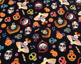 May include: Dark navy fabric with a repeating pattern of colorful sugar skulls, characters in sombreros, marigold flowers, and musical notes. The skulls have various designs and colors, including orange, pink, and blue. The fabric is likely cotton or a similar material.