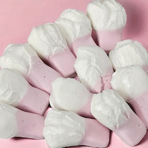 May include: A group of pink and white marshmallow candies shaped like teeth. The candies are arranged in a fan shape on a pink background.