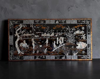 May include: A four-panel black lacquer wall art piece featuring intricate mother-of-pearl inlay depicting a rural landscape with figures, water buffalo, trees, and a boat. The rectangular frame has a gold-toned border with decorative patterns.