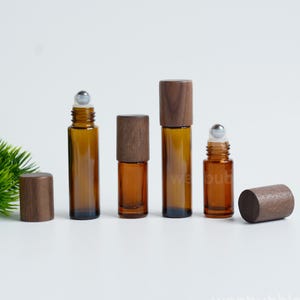 May include: Four amber glass roller bottles with dark wood caps and stainless steel roller balls. Two bottles are shown with the caps removed, revealing the roller mechanism, while two are capped. The text wenbubble is visible at the bottom.