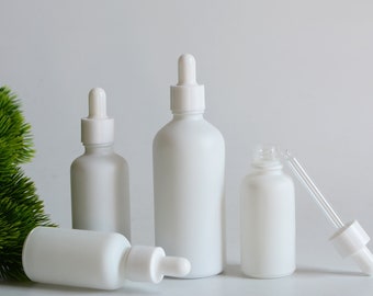 May include: Four white frosted glass bottles with droppers. The bottles are different sizes and are arranged on a white surface.
