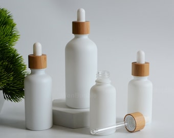 May include: Four white frosted glass bottles with bamboo lids and droppers. The bottles are different sizes and are arranged on a white surface.