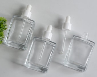 May include: Three clear glass bottles with white dropper tops. The bottles are square shaped and have a frosted finish. The droppers are made of clear glass and have a white rubber bulb.