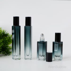 May include: Four glass rollerball bottles with black caps. The bottles are clear with a gradient of dark blue to light blue. The bottles are arranged in a row on a white surface.