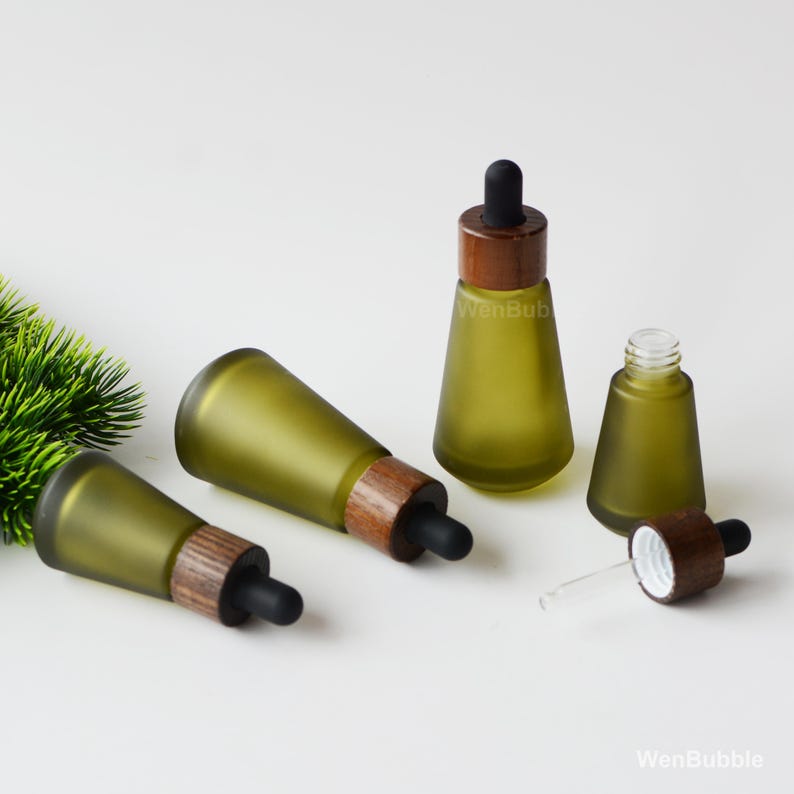 May include: Olive green glass dropper bottles with wooden collars and black rubber droppers. The bottles are in various positions, some upright and some lying down. The text "WenBub" is visible on the bottles.