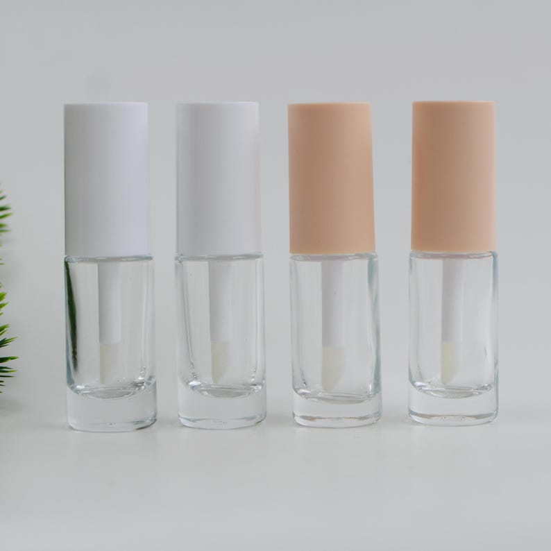 Peut inclure: Quatre flacons de gloss transparents avec des bouchons blancs et p&ecirc;che. Chaque flacon est dot&eacute; d'une baguette applicatrice transparente. Les flacons sont dispos&eacute;s en rang&eacute;e sur un fond blanc. Les bouchons sont cylindriques.