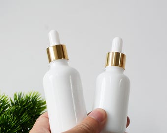 May include: Two white glass dropper bottles with gold lids. The bottles are empty and ready to be filled with essential oils, serums, or other liquids.