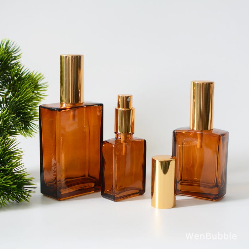 May include: Three amber glass bottles with gold spray tops. The bottles are of different sizes and are arranged in a row on a white surface.