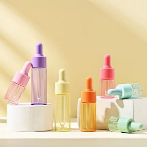 May include: A collection of colorful dropper bottles with pastel-colored tops in pink, purple, yellow, orange, and blue. The bottles are clear, showcasing the liquid inside. The background is a soft yellow, with a white block in the center.